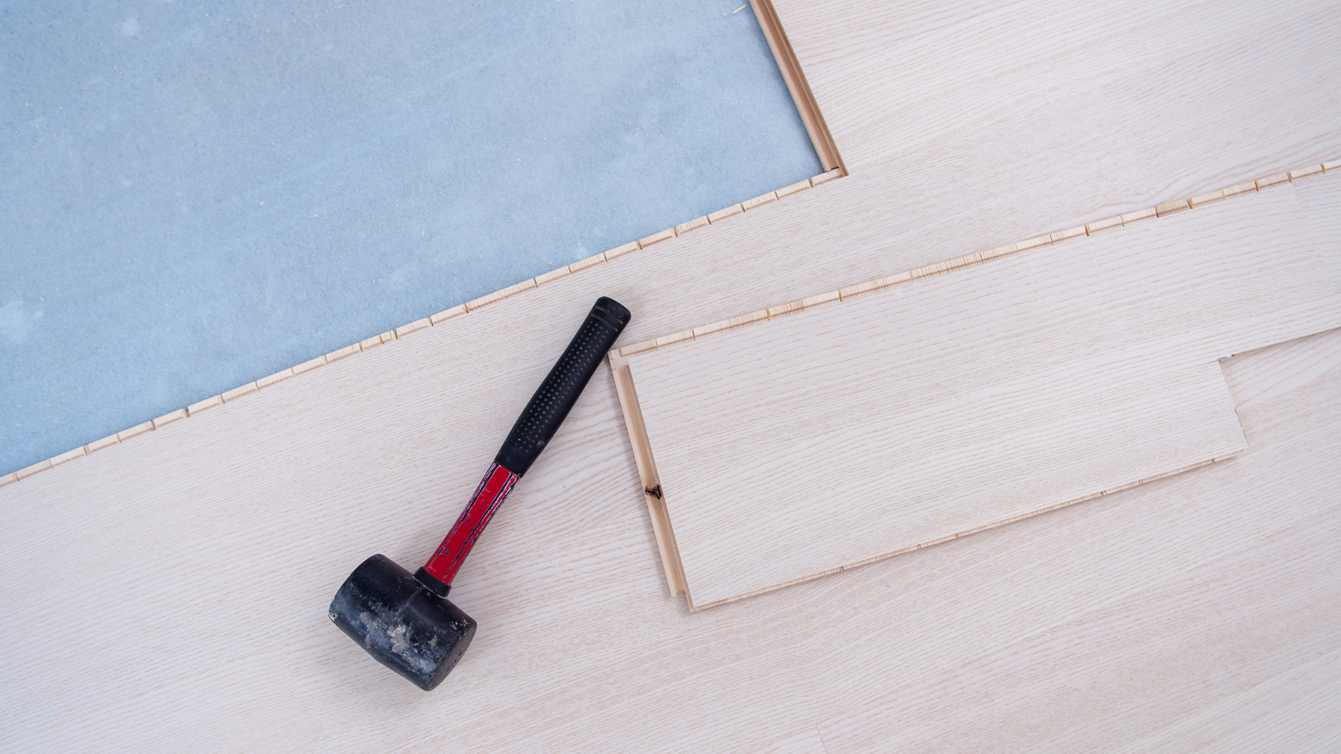 Professional installation of light wood laminate planks over a blue moisture barrier using specialized tools.