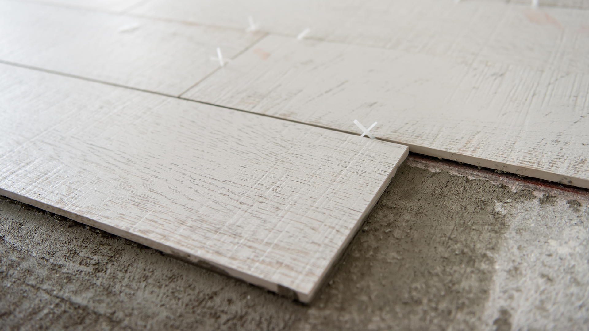 Professional installation of wood-look ceramic tiles using precision spacers on a prepared concrete substrate.